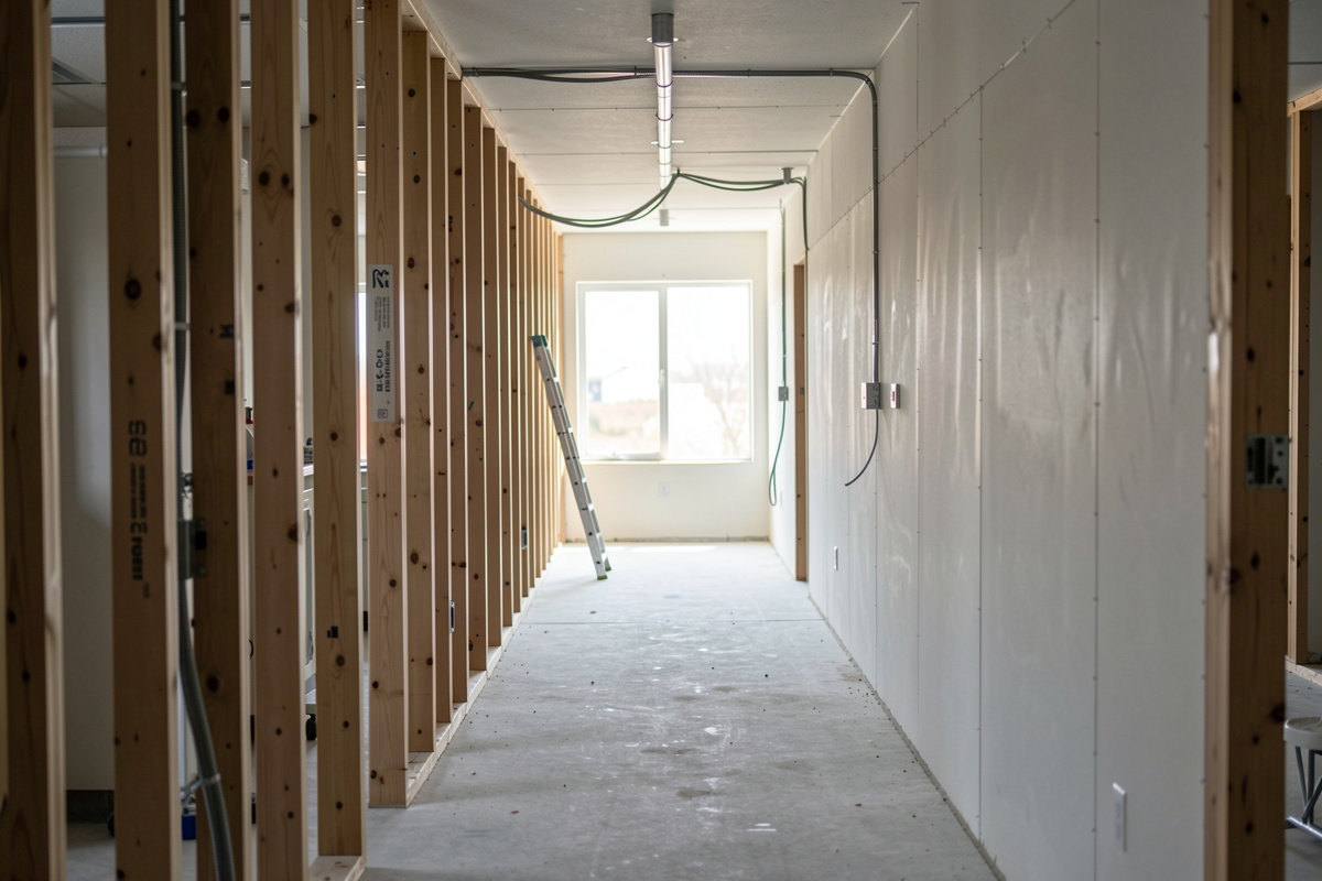 A dental office under construction seen from the corridor, bare stud walls and exposed conduit, daylight from a window at the far end, wide shot at eye level.