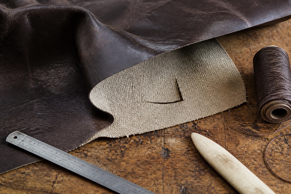 Dark leather panel turned back to show a short tear, woven backing and repair tools
