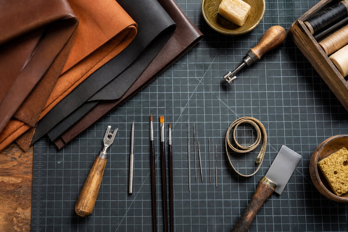 Leather repair tools, brushes, needles and folded hides arranged on a craft bench